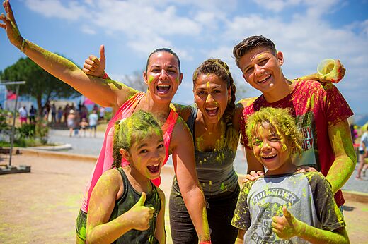 Familia sonriente cubierta de polvo de colores en una animación del camping CAPFUN Palombière en SAINT-NATHALENE.