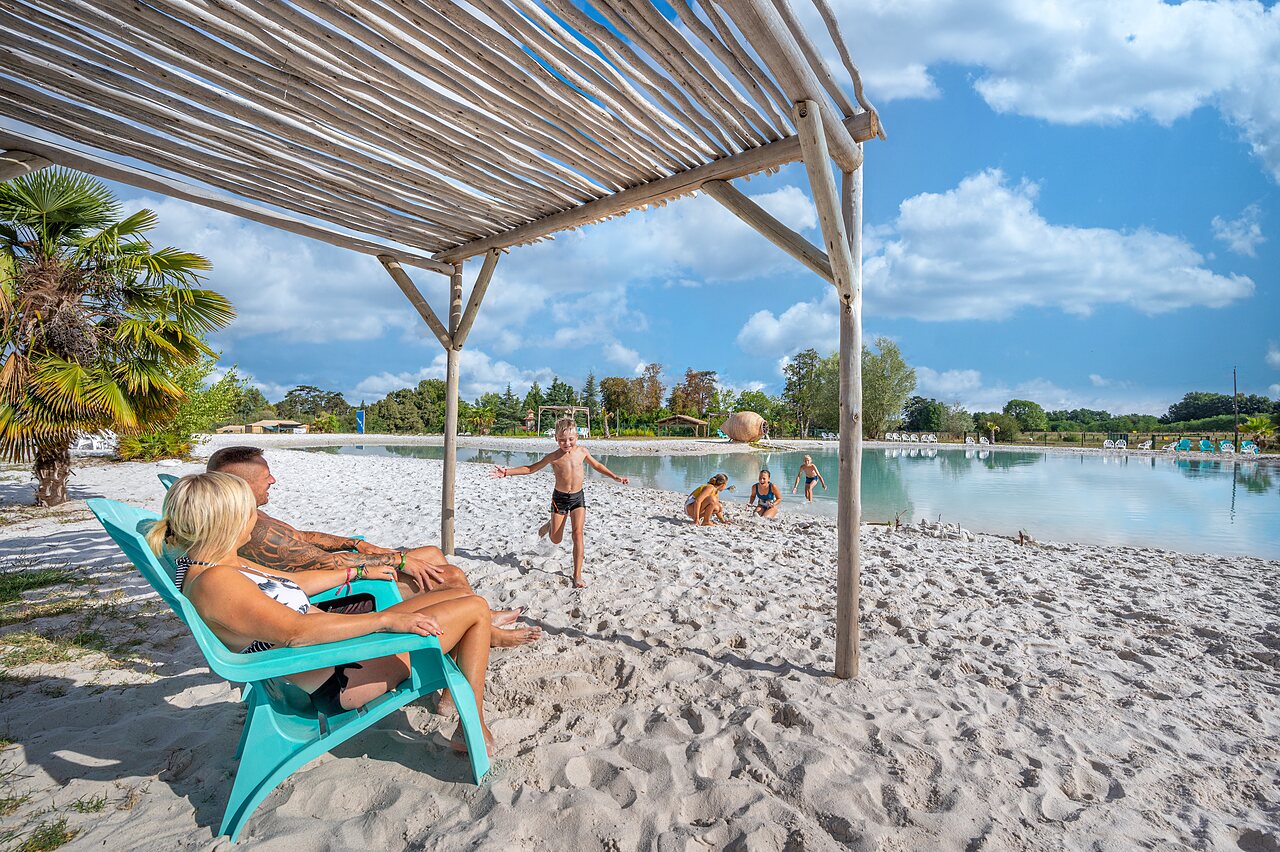 Familia disfrutando de la playa de arena y laguna en el camping CAPFUN Paradis de Bazas en BAZAS (33).