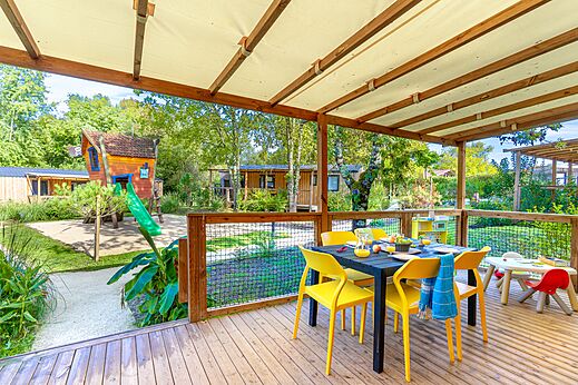 Terraza cubierta con mesa de comedor y zona de juegos en el camping CAPFUN Paradis de Bazas en BAZAS (33).