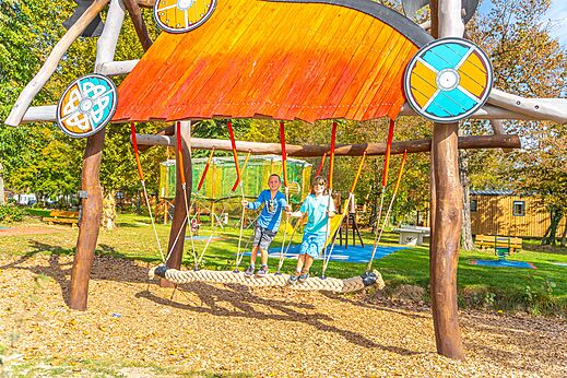 Niños sonrientes en un columpio gigante de cuerda en el camping CAPFUN Parc de Paris en Villevaudé (77).