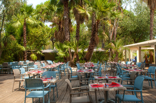 Restaurante exterior, mesas y sillas bajo palmeras, camping CAPFUN Parc et Plage.