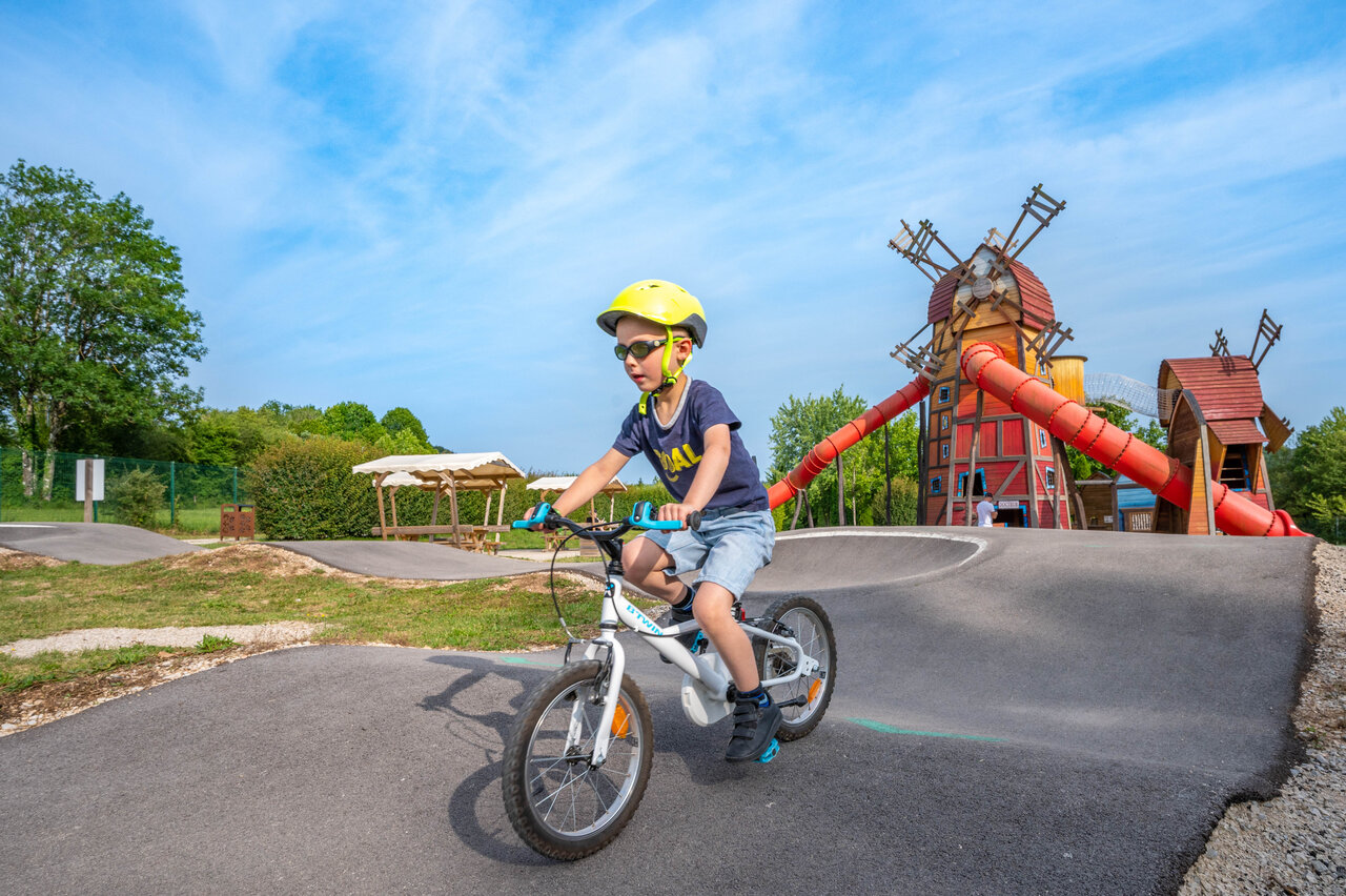 Ni�o en bicicleta en pump track con �rea de juegos molino en camping CAPFUN Pergola en Marigny (39).