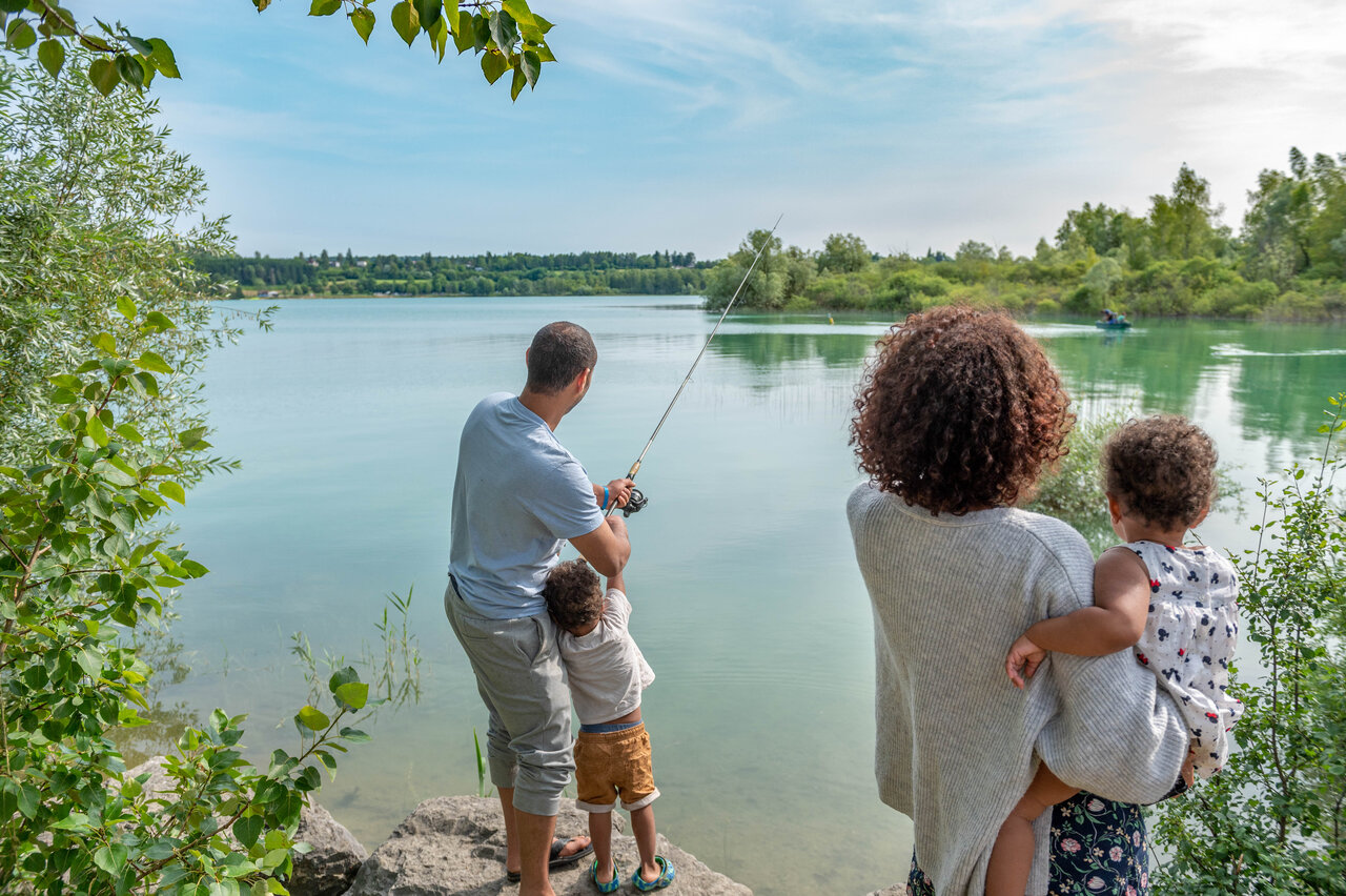 Familia pescando en orilla de lago tranquilo, naturaleza exuberante en camping CAPFUN Pergola en Marigny (39).