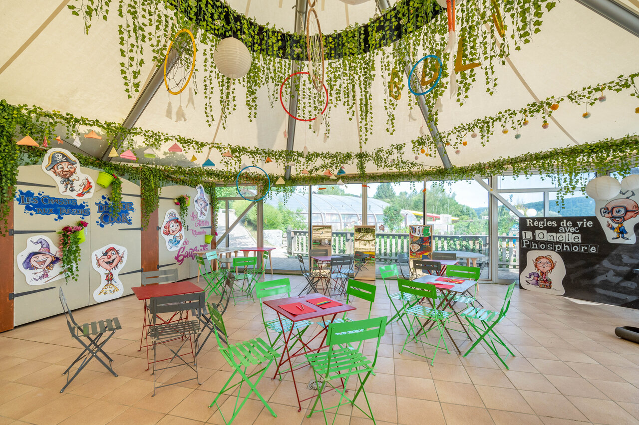 �rea de animaci�n infantil colorida con mesas y decoraciones en el camping CAPFUN Pergola en Marigny (39).
