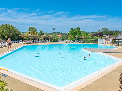 Gran piscina exterior con sillas y sombrillas en el camping CAPFUN Pergola en Marigny (39).