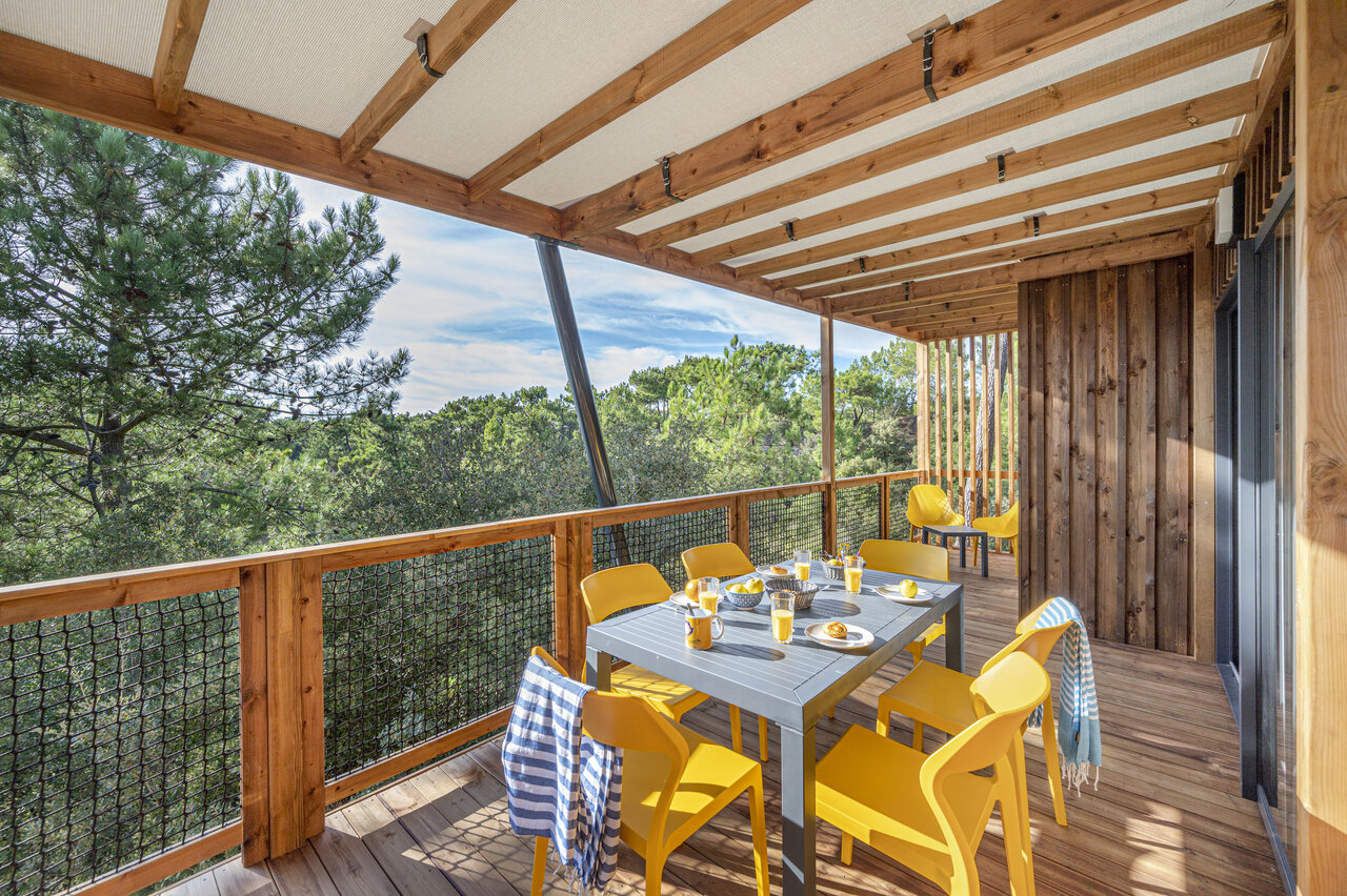 Terraza de Mobil-home con mesa y sillas amarillas, vista bosque en el camping CLICOCHIC Petit Bec en St Hilaire de Riez (85).