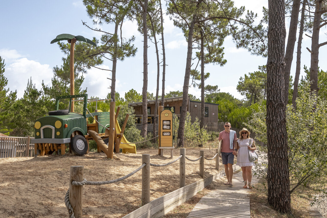 Zona de juegos con forma de jeep y pareja caminando en camping CLICOCHIC Petit Bec en St Hilaire de Riez (85).