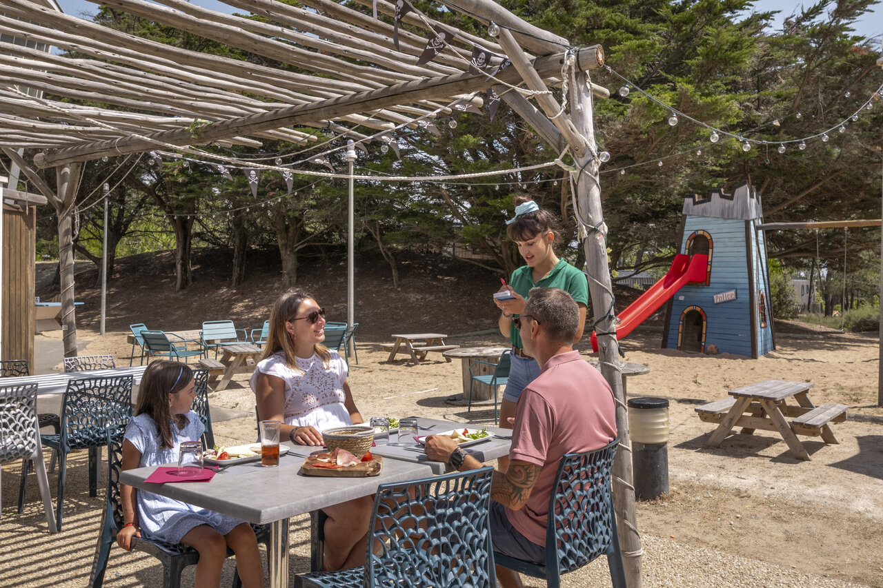 Familia almorzando en restaurante con zona de juegos en camping CLICOCHIC Petit Bec en St Hilaire de Riez (85).