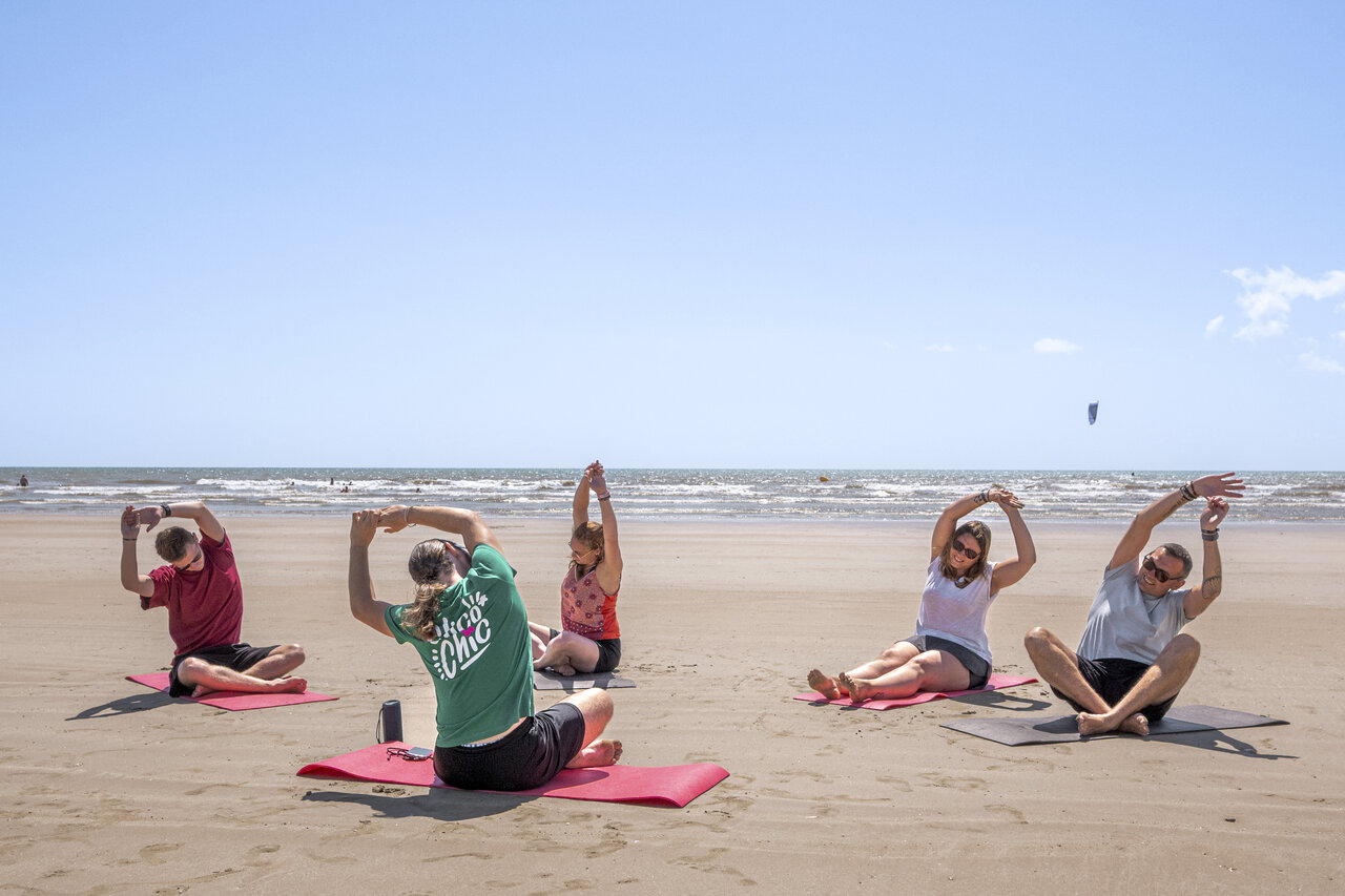Adultos practicando yoga en la playa en el camping CLICOCHIC Petit Bec.