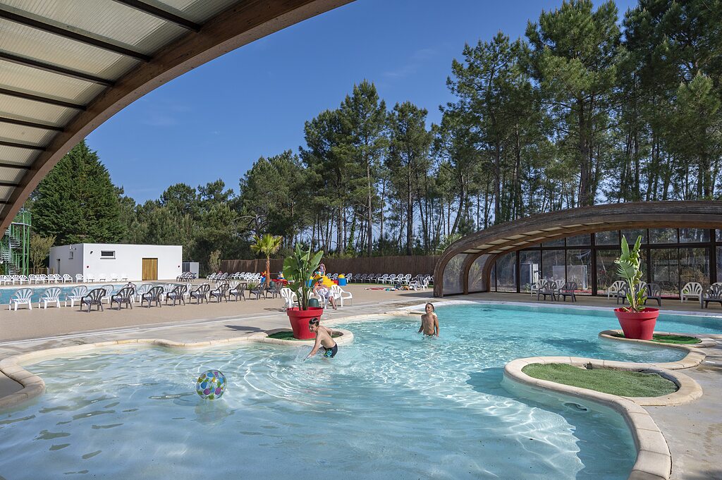 Piscina exterior con ni�os jugando y zona cubierta en camping CAPFUN Pin�da, CAZAUX (33).