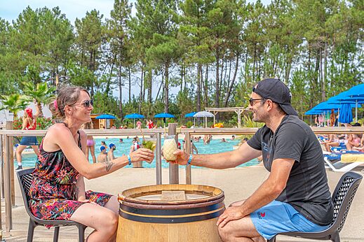 Pareja sonriente tomando una copa en el bar de la piscina del camping CAPFUN Pinèda en CAZAUX (33).