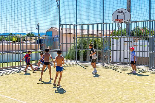 Niños jugando fútbol y baloncesto en cancha multideporte en camping CAPFUN La Pinède de Grimaud.