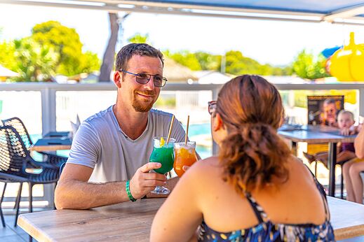 Pareja sonriente disfrutando cócteles en el bar del camping CAPFUN La Pinède de Grimaud.