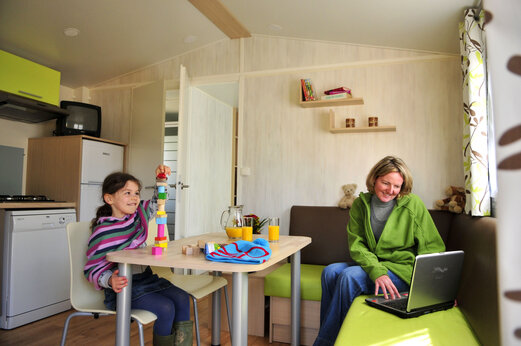 Interior de Mobil-home, niña jugando y mujer en CAPFUN Plan du Fernuy.