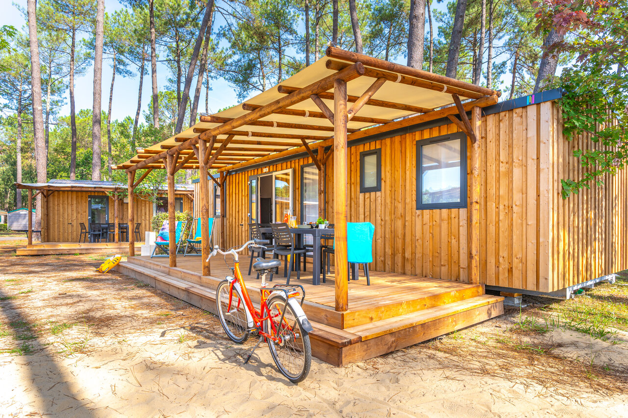 Mobil-home de madera con terraza cubierta y bicicleta, en el camping CAPFUN Pomme de Pin en Saubion (40).