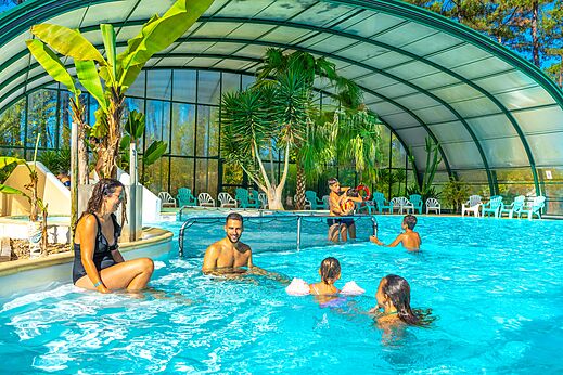 Piscina cubierta climatizada con palmeras y familia en el camping CAPFUN Pomme de Pin en Saubion (40).
