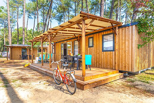 Mobil-home moderno con terraza cubierta y bicicleta en el camping CAPFUN Pomme de Pin en Saubion (40).