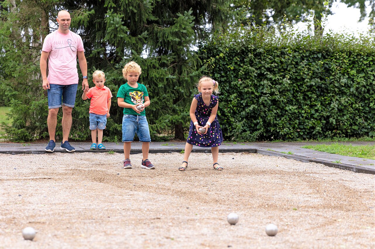 Familia jugando a la petanca en cancha dedicada en el camping CAPFUN Ponderosa en Ulicoten.