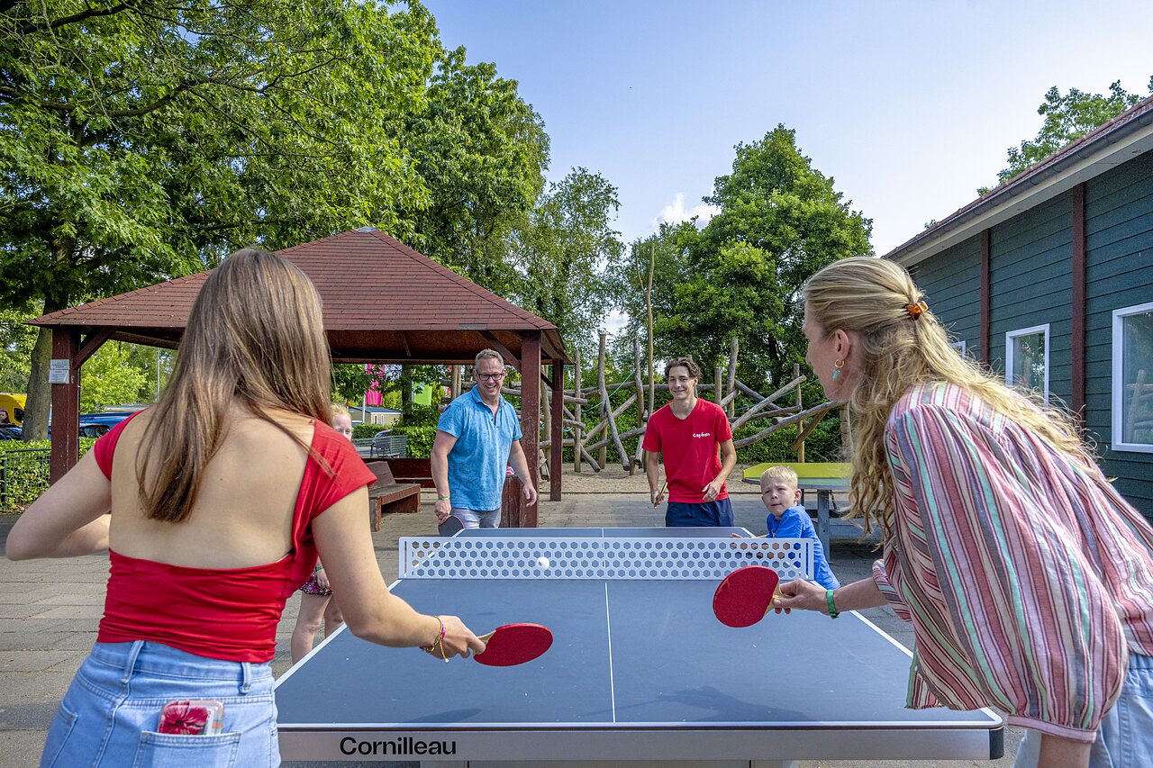 Familia jugando al tenis de mesa al aire libre en el camping CAPFUN Ponderosa en Ulicoten.