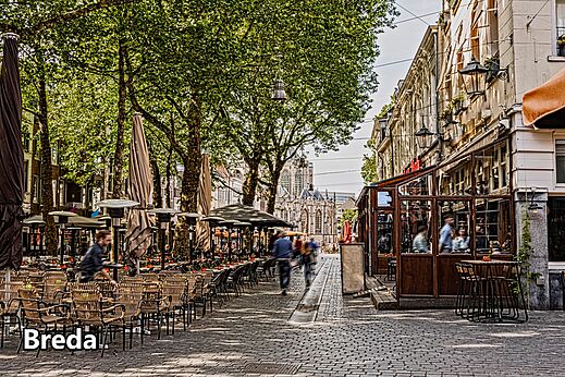 Calle animada con terrazas de café e iglesia histórica en Breda, Países Bajos.