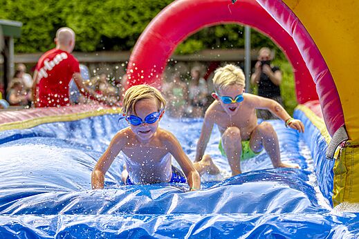 Niños divirtiéndose en un tobogán acuático inflable en el camping CAPFUN Ponderosa en Ulicoten.