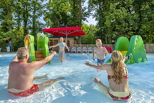 Piscina exterior con juegos acuáticos y familia divirtiéndose en el camping CAPFUN Ponderosa en Ulicoten.