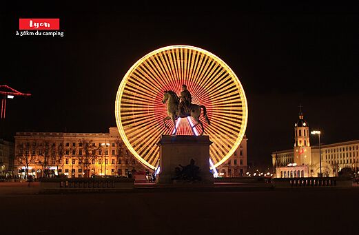 Noria iluminada y estatua ecuestre en Lyon, ciudad para visitar en Ródano-Alpes.