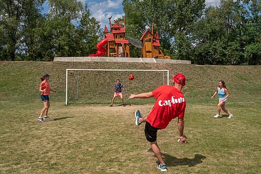 Familia jugando al fútbol en campo deportivo con zona de juegos en camping CAPFUN Les Portes du Beaujolais en Anse (69).