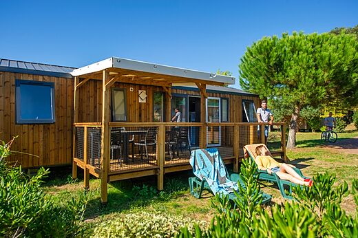 Mobil-home de madera con terraza cubierta y sillas en el camping CAPFUN Quatre Vents d'Ol�ron en St Georges d'Ol�ron (17).
