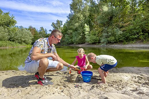 Familia jugando en la arena junto al agua en CAPFUN Rakelbos, Westelbeers.