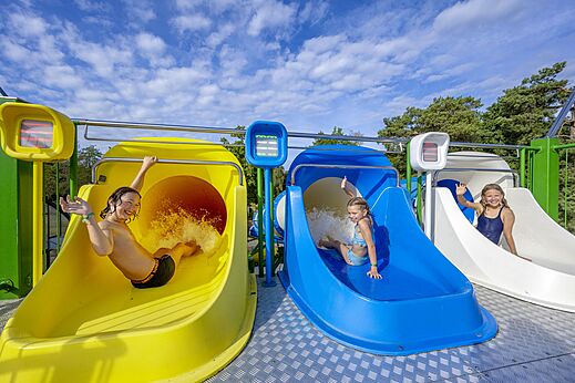 Ni�os divirti�ndose en los toboganes acu�ticos coloridos del camping CAPFUN Rakelbos en Westelbeers.