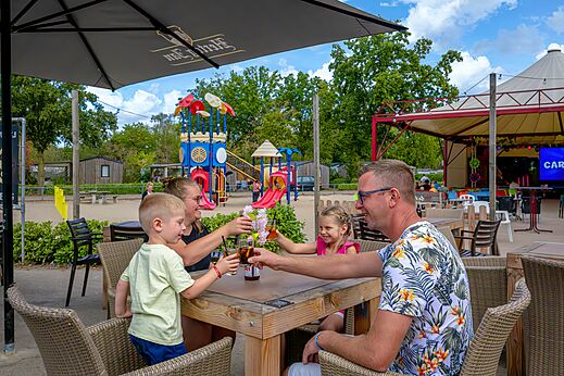 Familia disfrutando del bar y zona de juegos en el camping CAPFUN Rakelbos en Westelbeers.