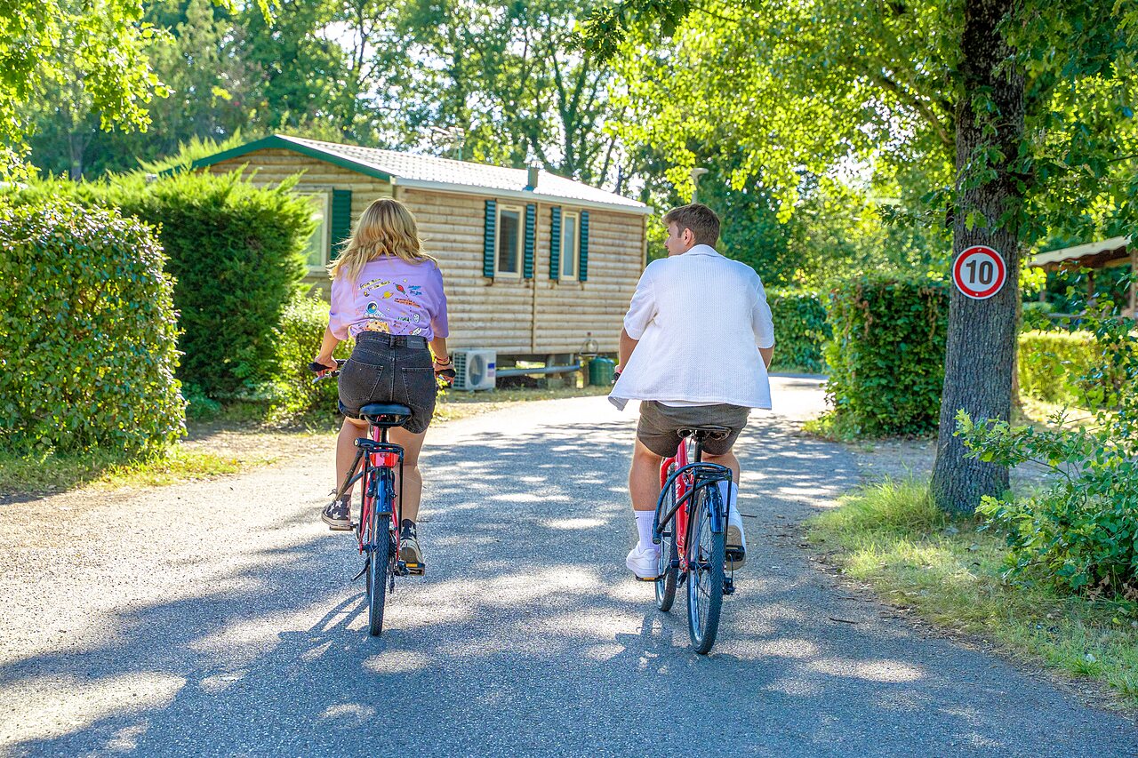 Pareja en bicicleta frente a Mobil-home en camping CAPFUN R�gni�re, VILLETTE D'ANTHON (38).