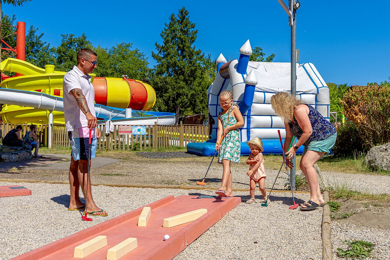 Familia jugando minigolf con toboganes acu�ticos y castillo hinchable en camping CAPFUN R�gni�re en VILLETTE D'ANTHON (38).
