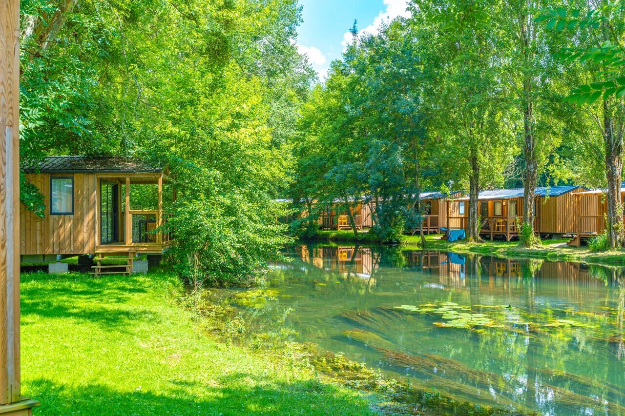 Mobil-homes de madera junto a un r�o verde, naturaleza exuberante en el camping CAPFUN La Rivi�re en Valence-en-Poitou (86).