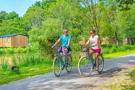 Pareja en bicicleta por sendero verde junto a estanque en camping CAPFUN La Rivi�re en Valence-en-Poitou (86).