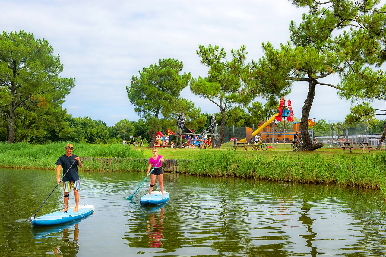 Paddleboarders en el agua, zona de juegos infantiles en camping CAPFUN Roumingue en LANTON (33).