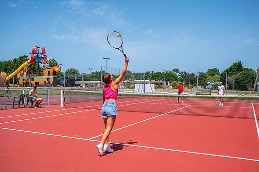 Cancha de tenis roja con jugadores en camping CAPFUN Roumingue, LANTON (33).