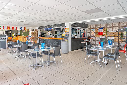 Bar y zona de restaurante con mesas y sillas en el camping CAPFUN Saint Laurent en LA FORET FOUESNANT (29).