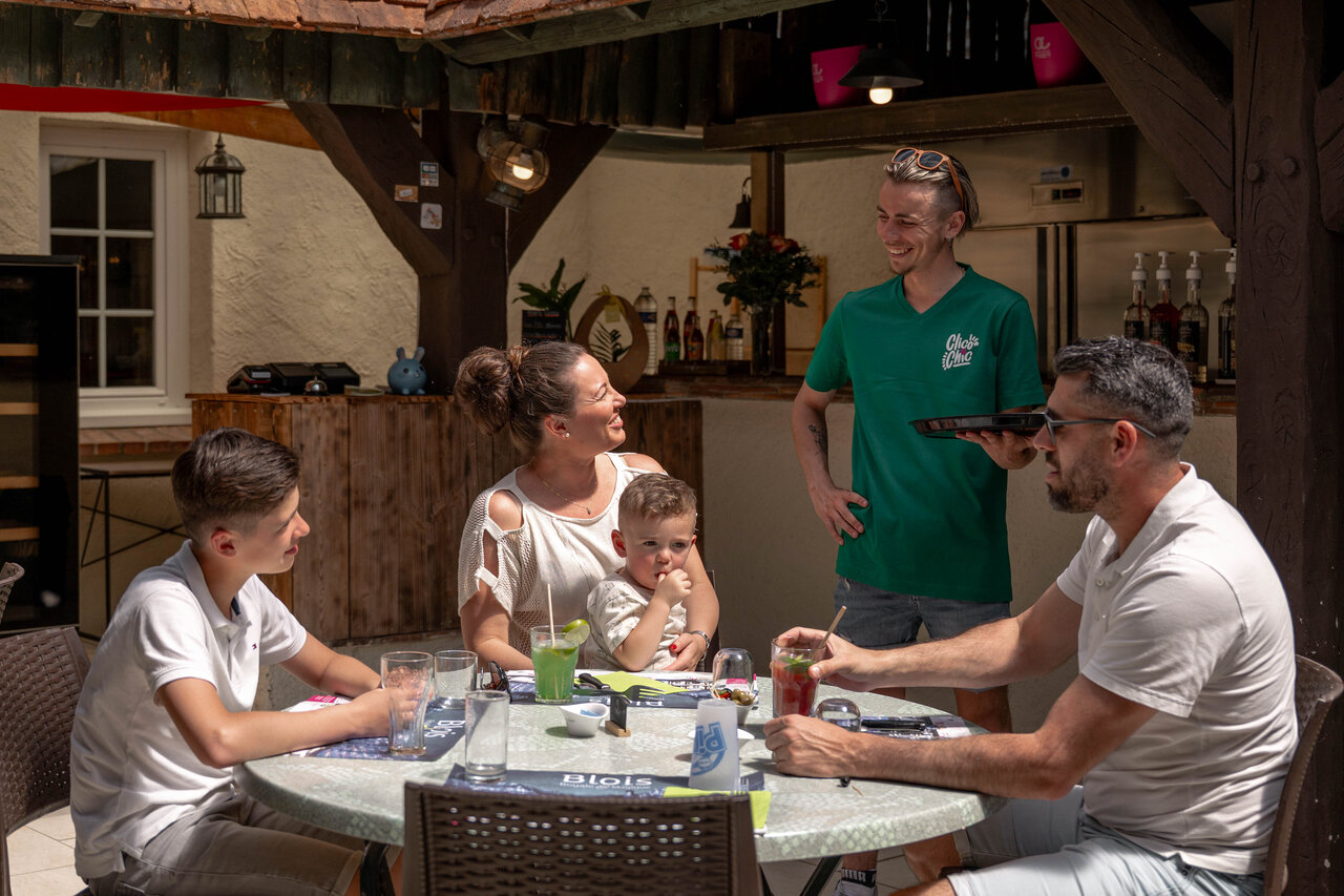 Restaurante-bar exterior animado con familia en el camping CLICOCHIC Les Saules de Cheverny.