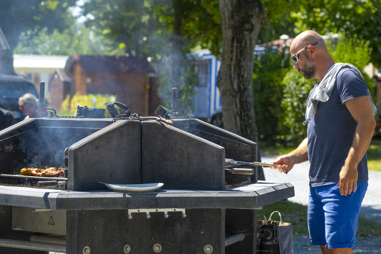 Parrillada en barbacoa com�n, hombre cocinando en el camping CLICOCHIC Seuli�res en Saint-Denis-d'Ol�ron.