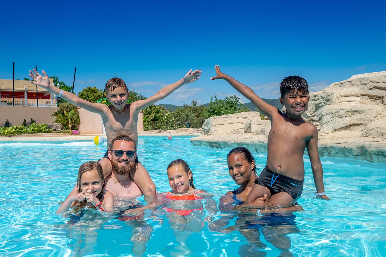 Familia sonriente disfrutando de la piscina exterior en el camping VAGUES OCEANES Soleil de Provence.