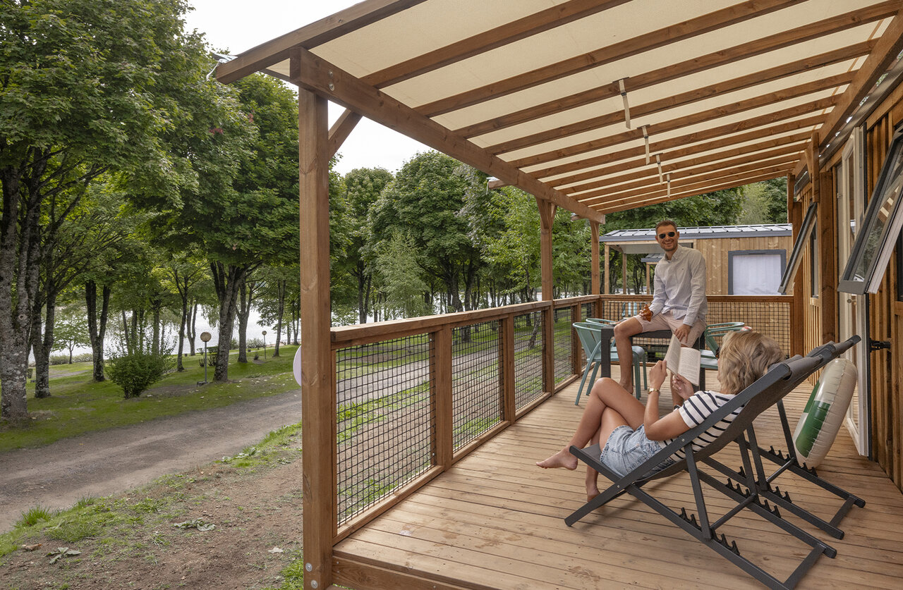 Pareja en terraza Mobil-home de madera, vista lago, en camping CLICOCHIC Soleil Levant.
