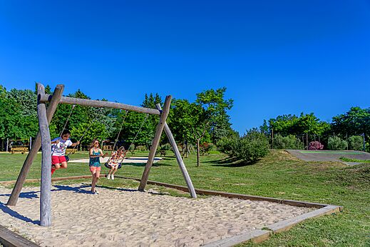 Columpio de madera con niños jugando en la arena en el camping CAPFUN Soubeyranne en REMOULINS (30).