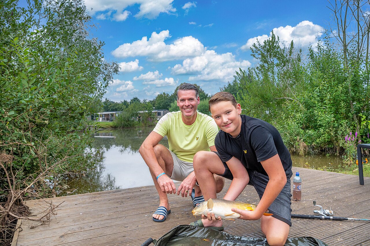 Padre e hijo sonrientes con una carpa pescada en el estanque en el camping CAPFUN Vakantiepark Capfun het Stoetenslagh en Rheezerveen.
