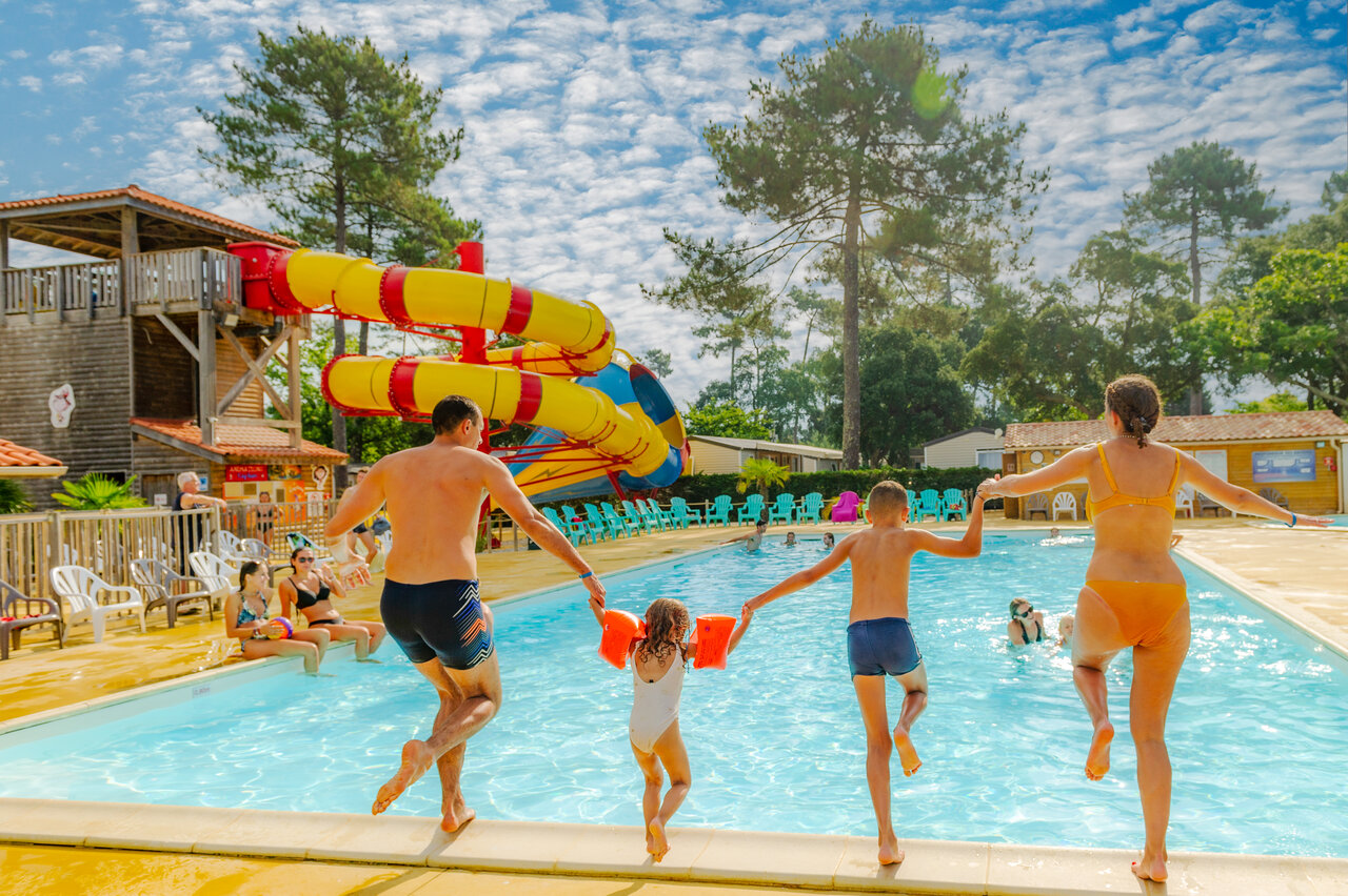 Familia saltando a la piscina con toboganes gigantes en el camping CAPFUN Sud Land en Labenne-Ocean.