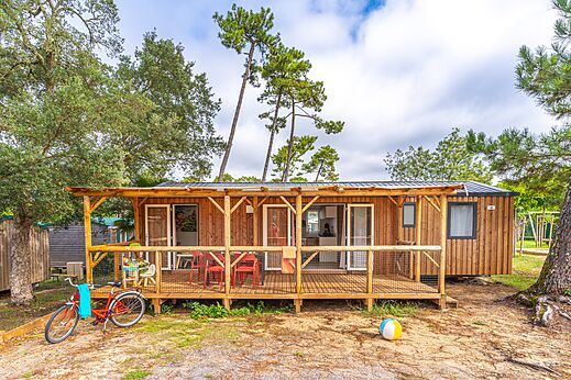 Mobil-home de madera con terraza cubierta y bicicleta en el camping CAPFUN Sud Land en Labenne-Ocean (40).