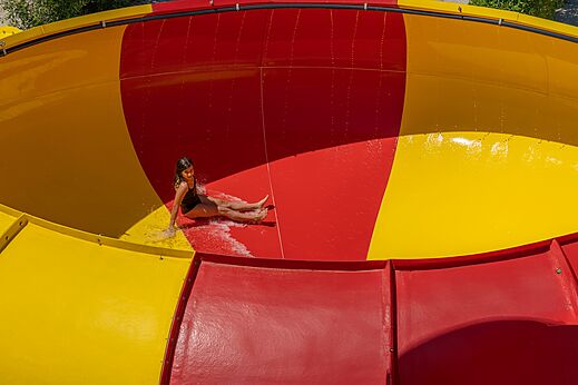 Niña deslizándose por tobogán acuático rojo y amarillo en CAPFUN Talaris Vacances en Lacanau (33).