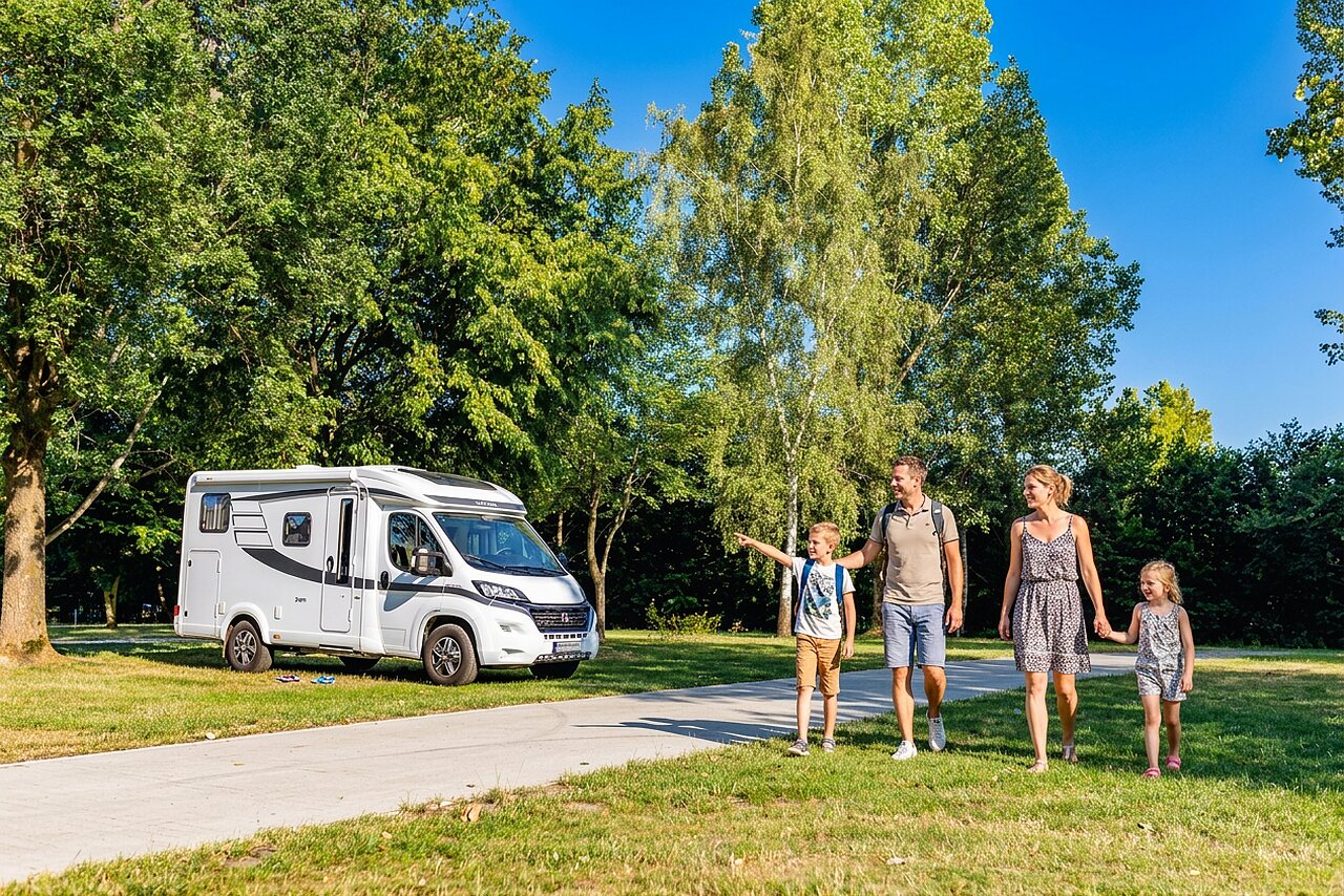 Familia y autocaravana blanca en parcela verde en el camping CAPFUN Tecklenburg en Tecklenburg-Leeden (49).