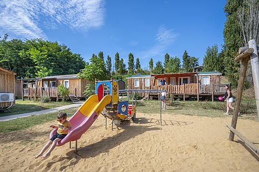 Zona de juegos con tobogán y Mobil-homes en camping CAPFUN Temps Libre en BOUGE CHAMBALUD.